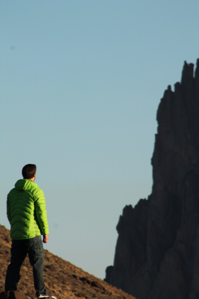 Photo of a man in a green puffer jacket that looks at Shiprock. Image links a gallery of shiprock photos.